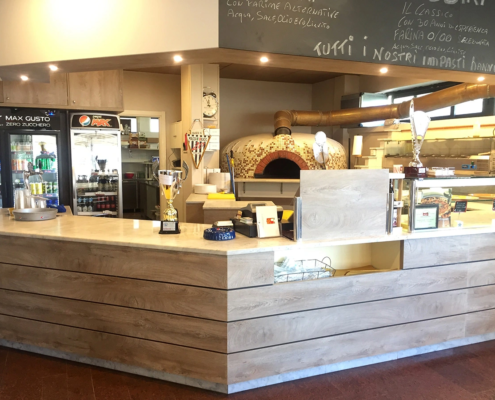 Arredamento su misura della pizzeria Ale's Pizza, bancone in legno chiaro e veduta sul forno della pizzeria