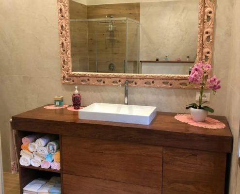 Arredamento su misura per bagno, mobile di design in legno scuro con specchio artigianale visto frontalmente.