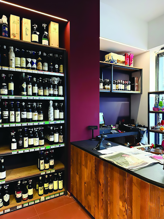 arredamento-vineria-bancone-e-scaffali Bancone, cassa e scaffali con i vini in esposizione all'interno di una vineria.