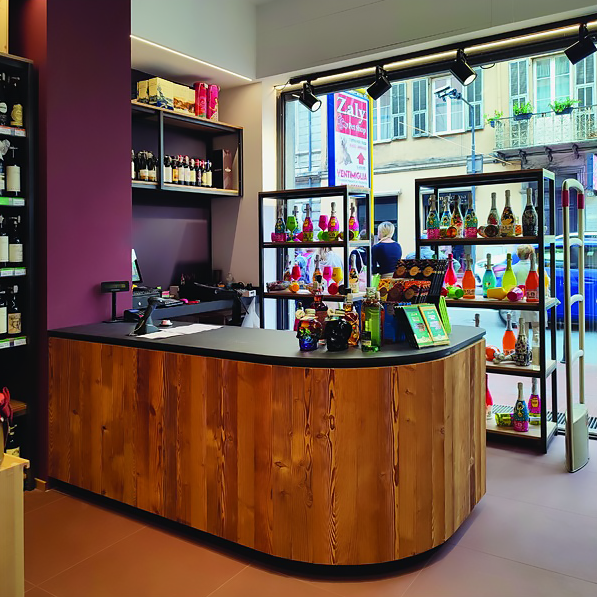 arredamento-vineria-bancone-su-misura Vista frontale di un bancone/cassa realizzato in legno e con una copertura nera all'interno di una vineria.