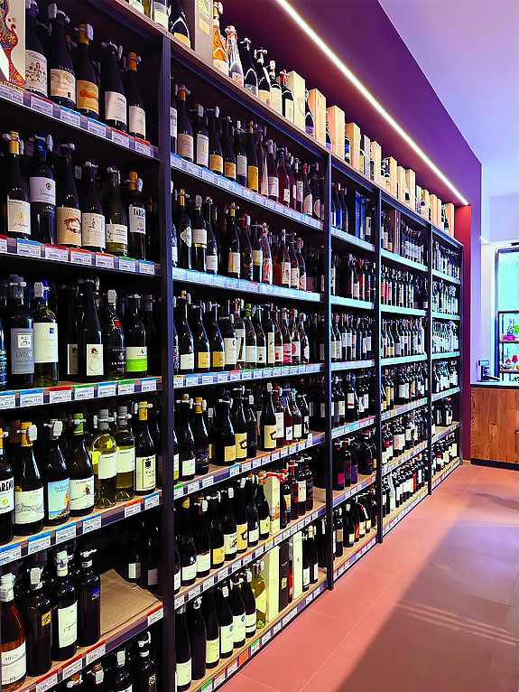 arredamento-vineria-scaffalature-personalizzate Scaffalature in metallo e legno chiaro con vini esposti all'interno di una vineria.